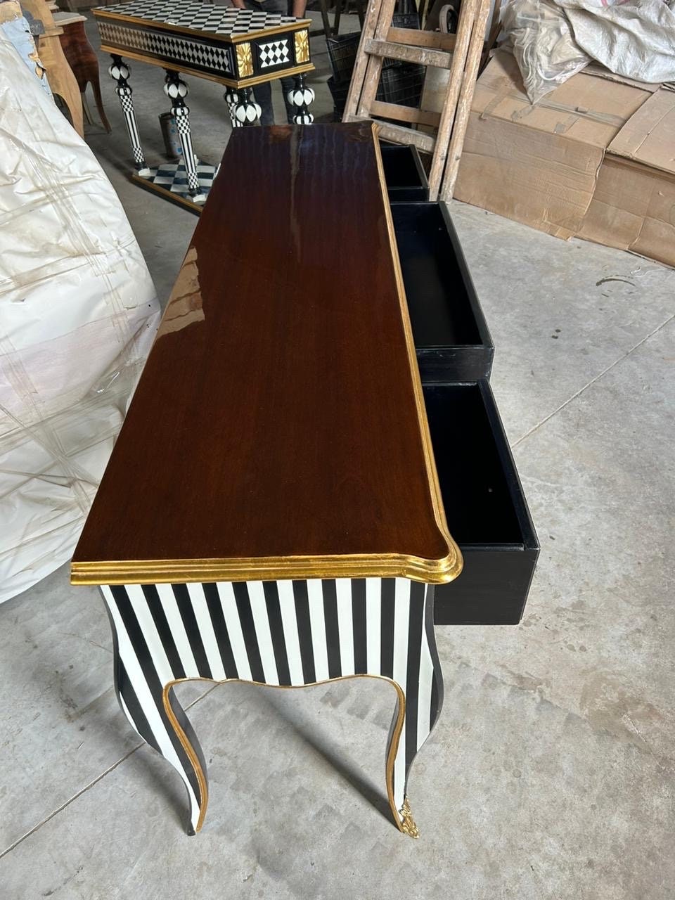 May include: A black and white striped console table with gold accents and three drawers. The table has a wooden top and ornate legs.