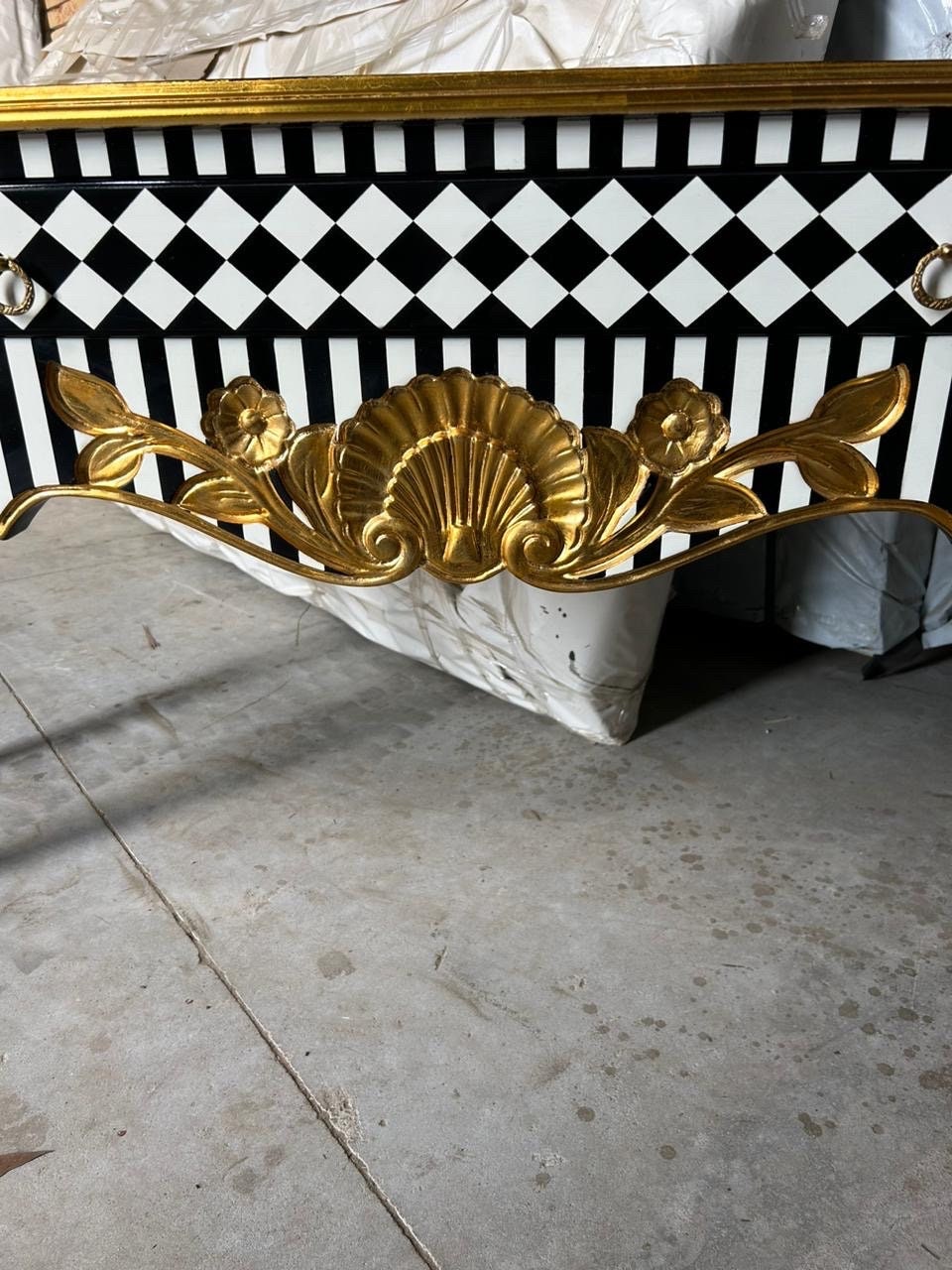 May include: A black and white checkered and striped console table with gold accents and a decorative shell design. The table has a gold trim and a scalloped edge.