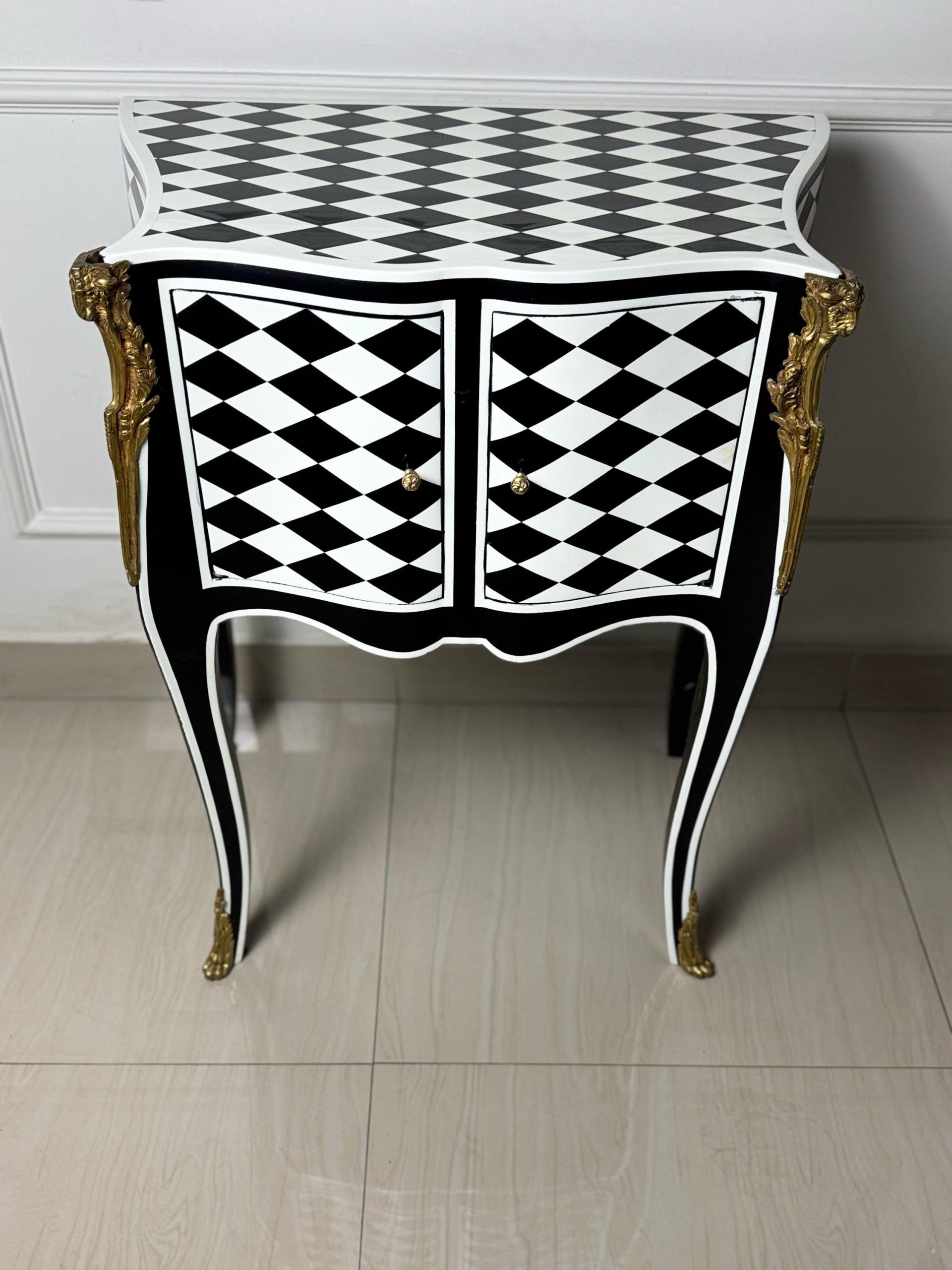May include: A black and white checkered side table with gold accents and two doors. The table has a curved top and legs.