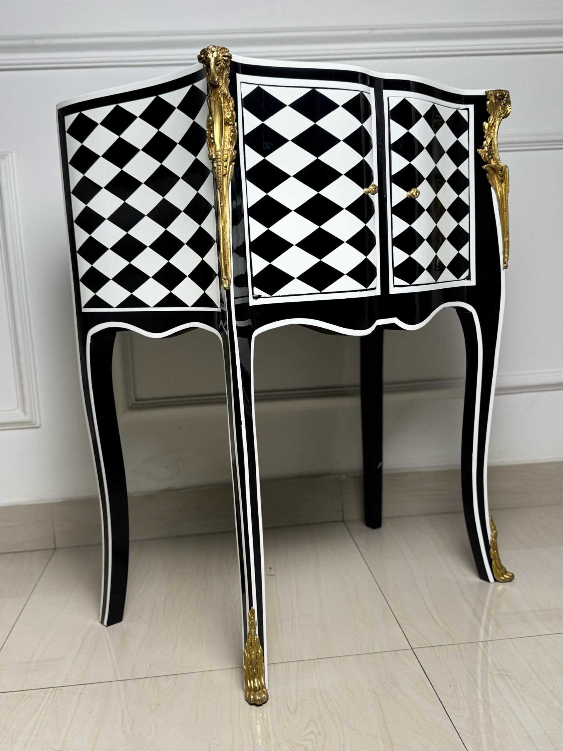 May include: A black and white checkered side table with gold accents. The table has two doors and sits on four legs.