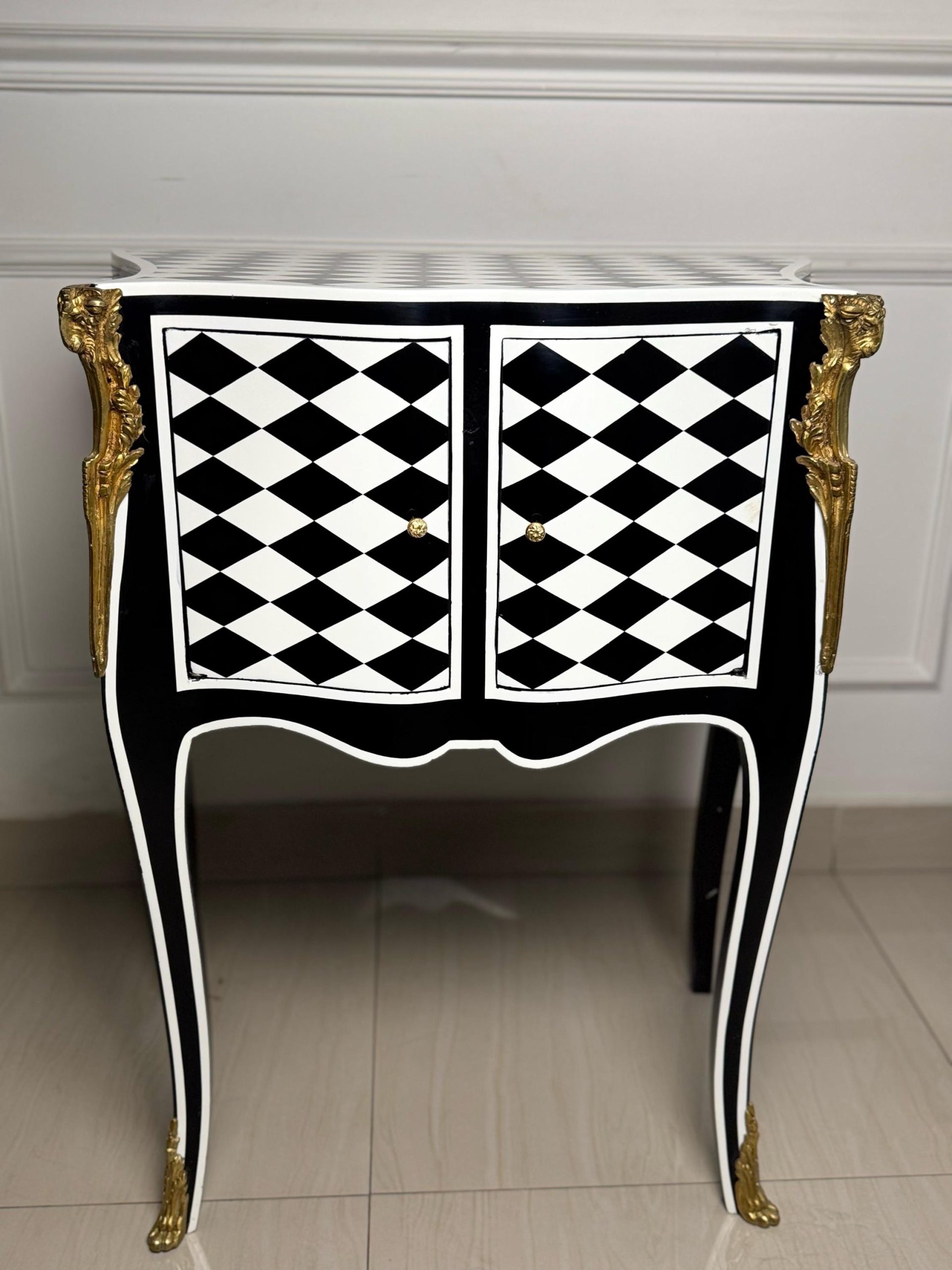 May include: A black and white checkered cabinet with gold accents and ornate legs. The cabinet has two doors and a top surface.