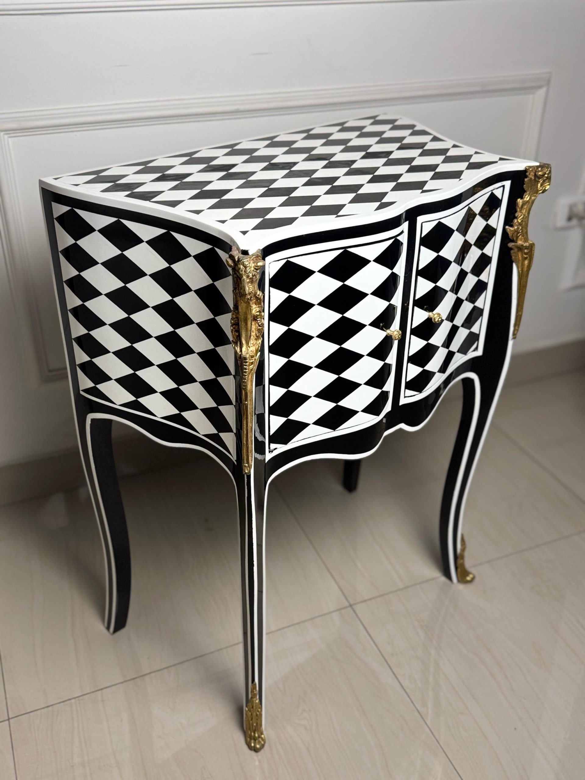 May include: A black and white checkered side table with gold accents. The table has two doors and sits on four legs with gold feet.