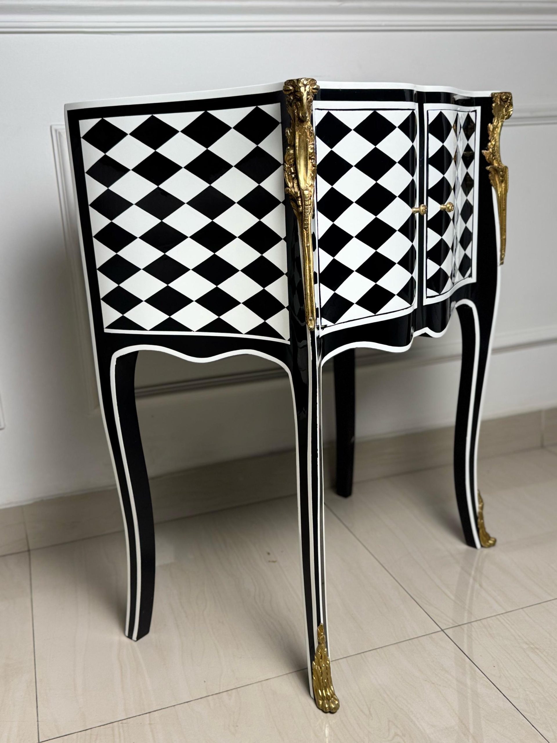 May include: A black and white checkered side table with gold accents and ornate legs. The table has two doors and a curved top.