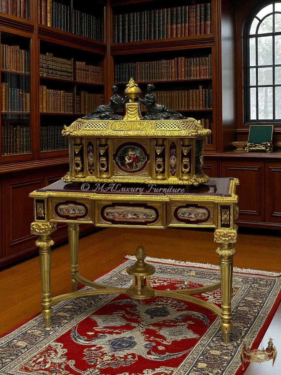 May include: A gold and black antique cabinet with intricate detailing, featuring a decorative top with two figures and a central finial. The cabinet sits on a matching table with ornate legs, placed on a red patterned rug. The background shows a library with bookshelves.
