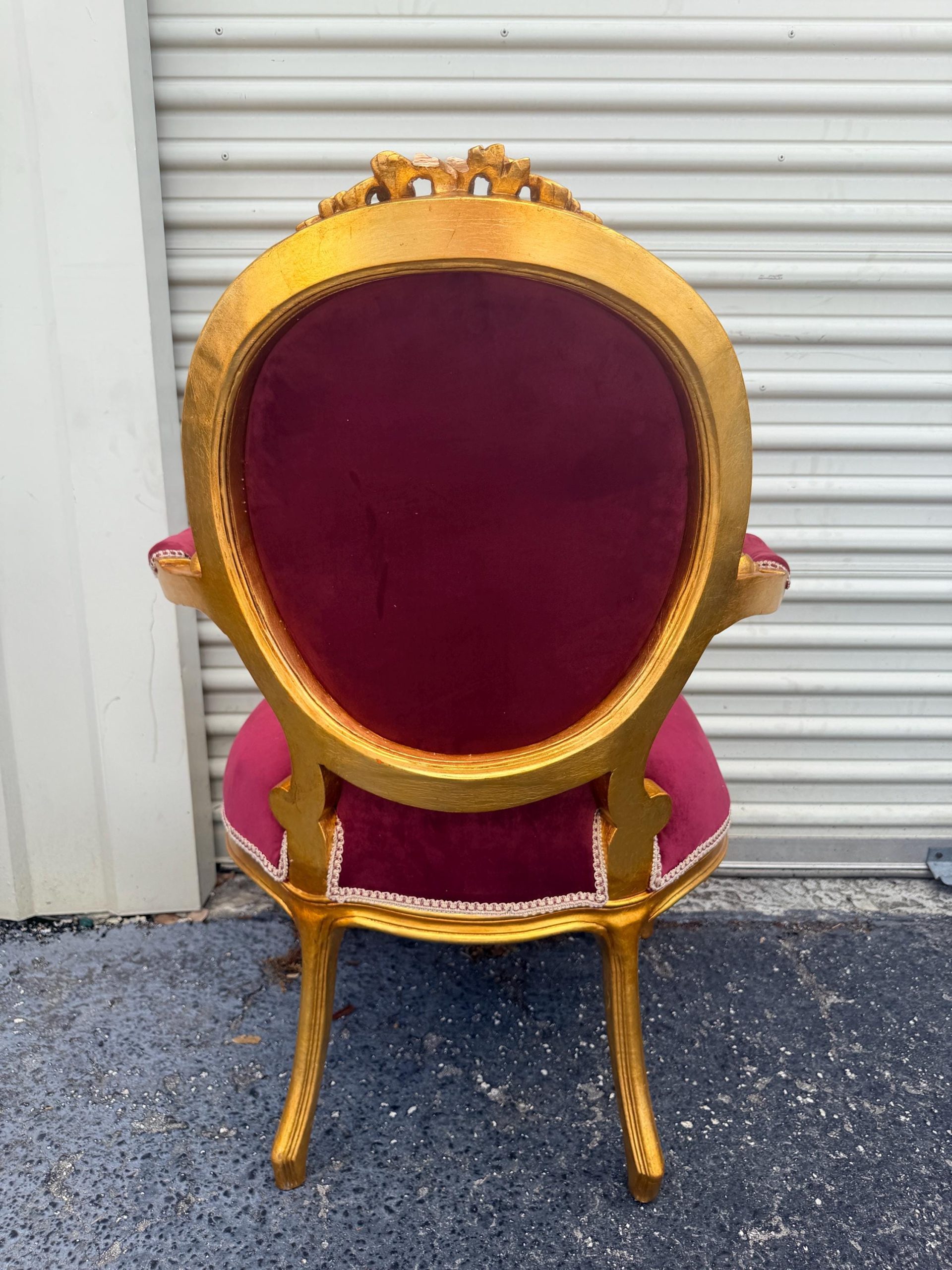 May include: A gold-framed chair with a burgundy velvet seat and back. The chair has ornate detailing on the frame and legs. The back of the chair is oval-shaped, and the seat is a matching burgundy color.