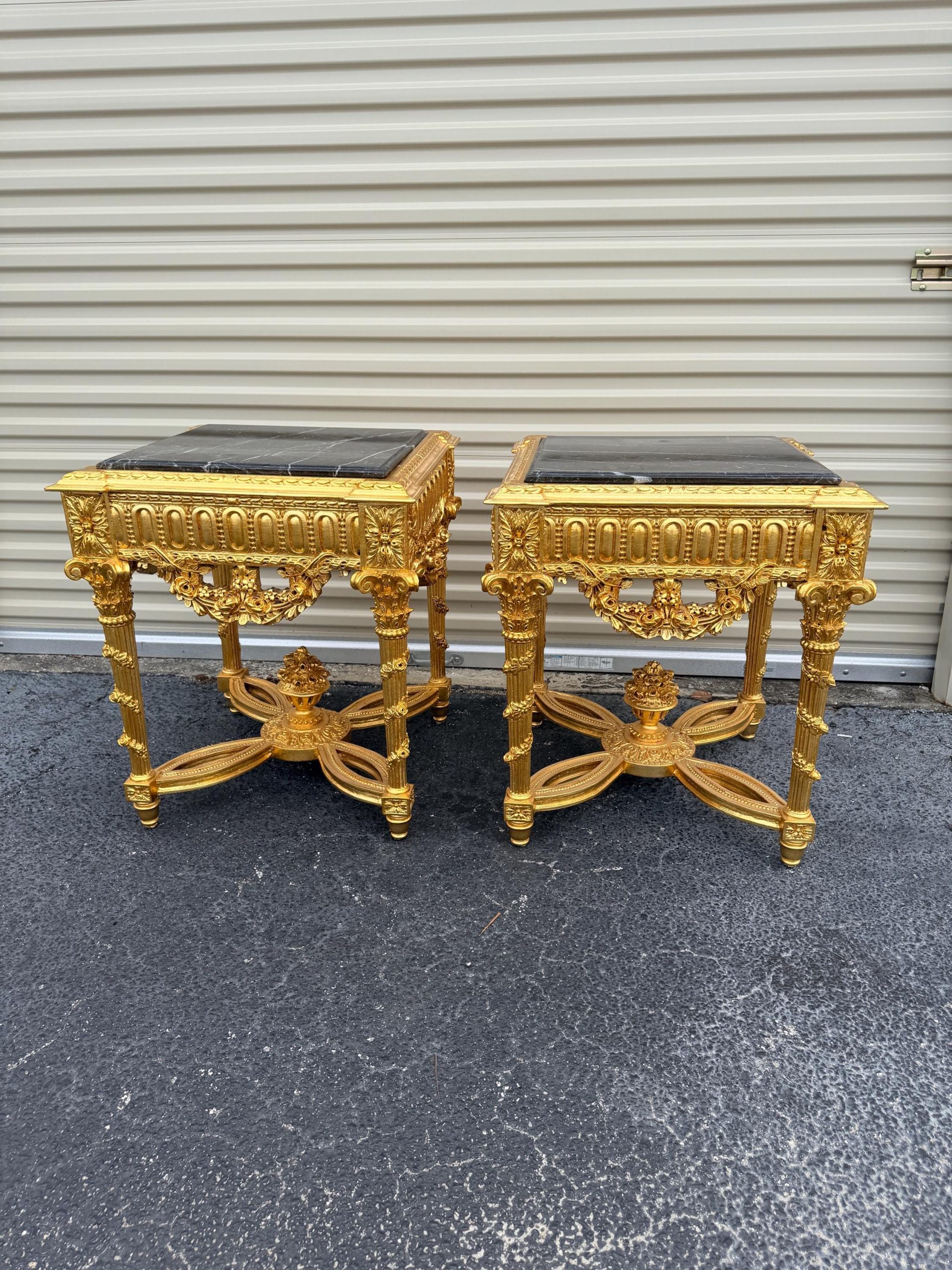 May include: Two ornate, gold-colored side tables with black marble tops. The tables feature intricate carvings and decorative legs. The tables are likely antique or vintage, adding a touch of luxury to any room.
