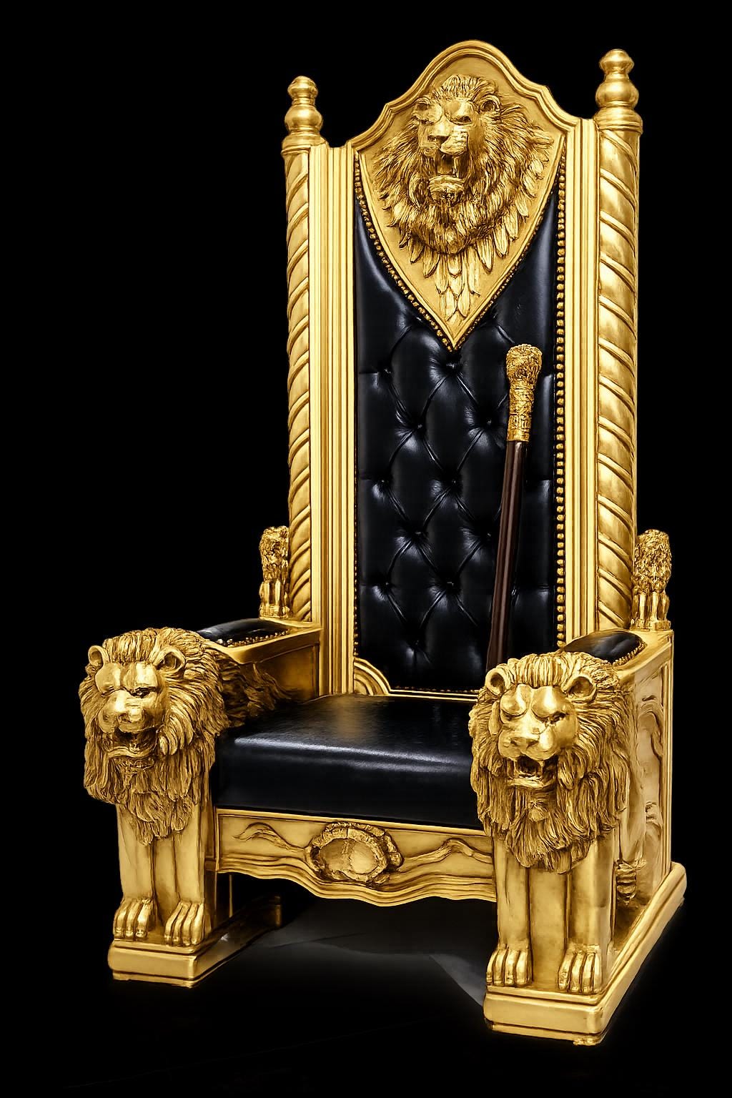May include: A high-backed throne chair featuring a gold-painted frame with carved lion heads on the armrests and top crest. The seat and backrest are upholstered in black tufted leather. A dark wooden cane with a gold handle rests against the back.