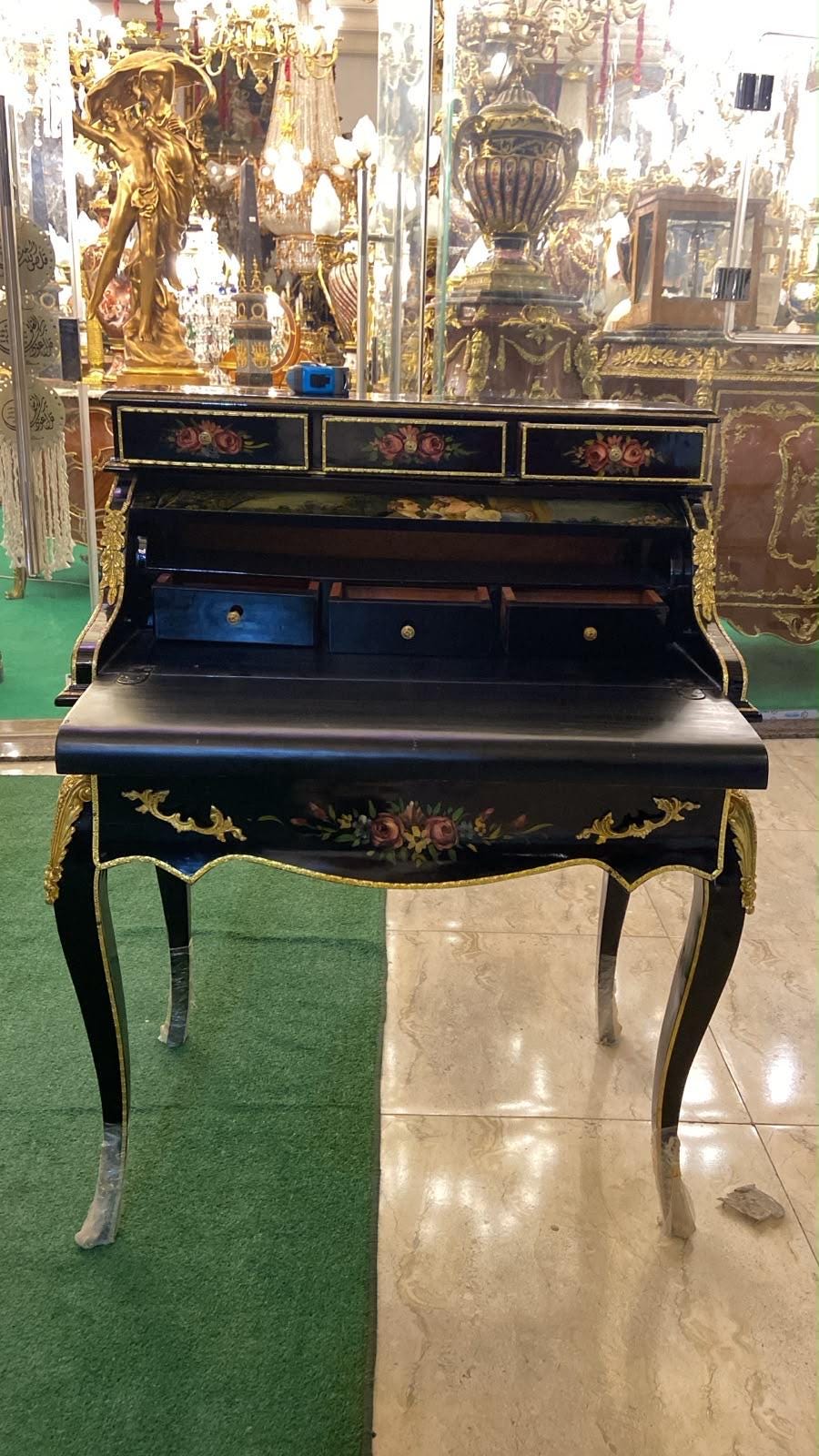 May include: A black secretary desk featuring gold metal accents, floral hand-painted motifs on the drawer fronts, and a drop-down writing surface. The desk includes three upper drawers, three interior drawers, and curved legs with gold trim details.