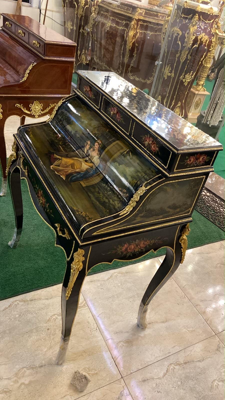 May include: A black lacquered roll-top desk featuring hand-painted floral motifs and a central scene depicting two figures in a landscape. The desk is accented with gold-toned metal hardware and ornate carvings on the four curved legs.