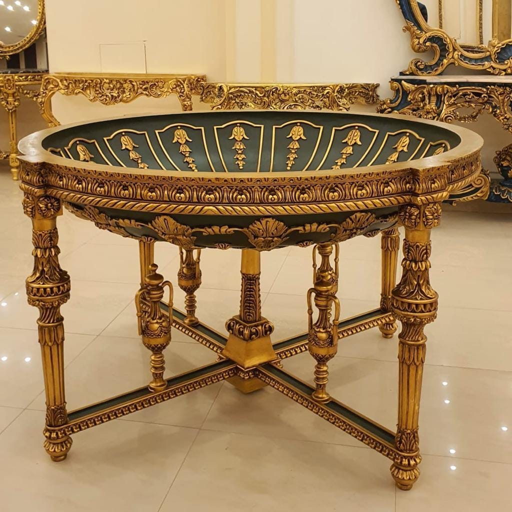 May include: A round table with a deep, dark green basin featuring gold-painted floral carvings along the interior rim. The table is supported by four ornate, gold-finished legs with intricate detailing and a central cross-brace structure.