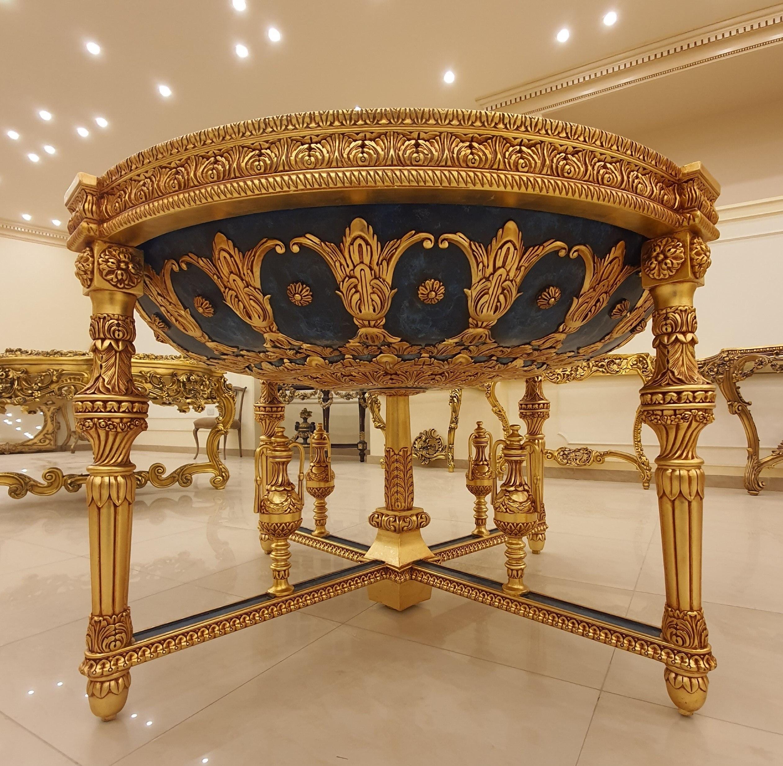 May include: A round table featuring a deep blue basin with intricate gold leaf carvings and floral motifs. The table is supported by four ornate gold legs connected by a central cross-shaped base with decorative finials and detailed scrollwork.