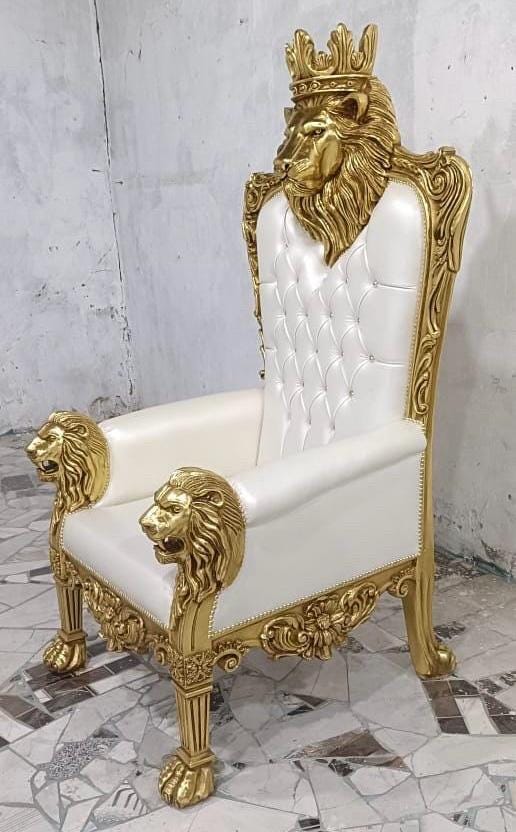 May include: A high-back throne chair featuring a gold-painted wooden frame with carved lion head armrests and a large lion head crest at the top. The seat and backrest are upholstered in white tufted material with small embedded crystal accents.