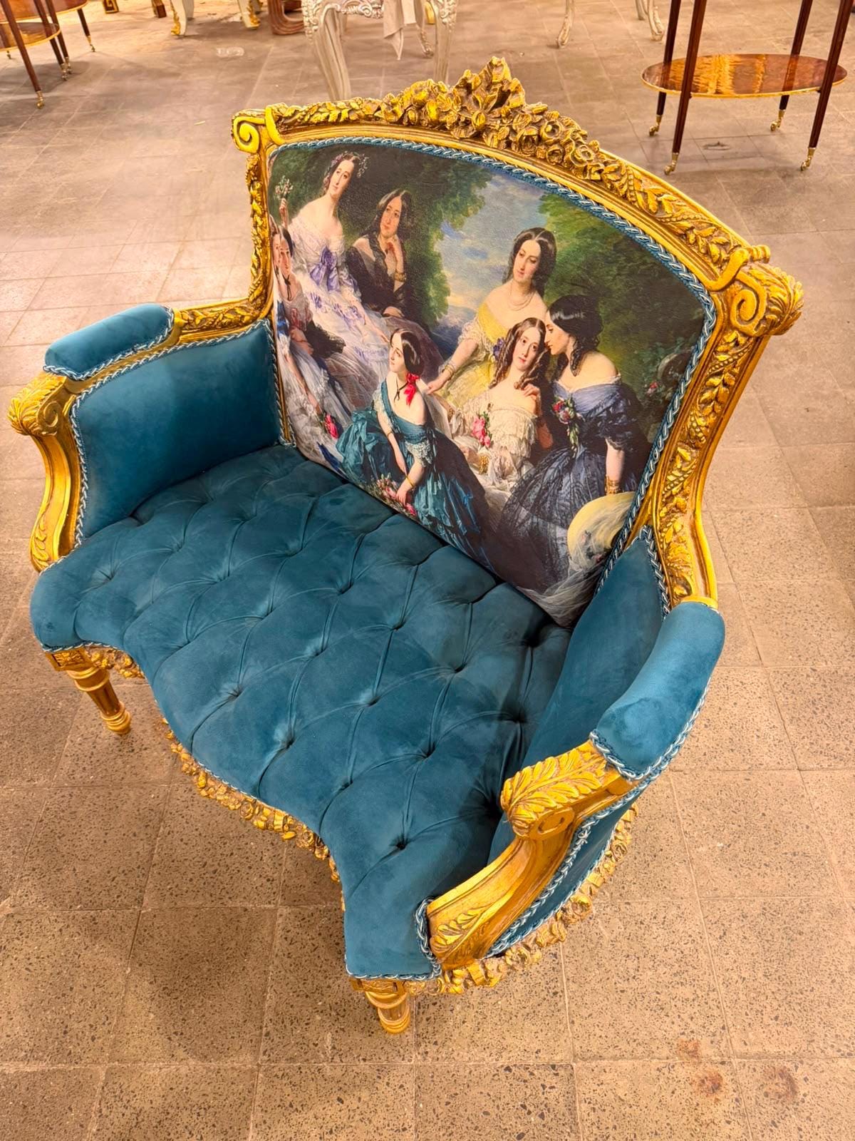 May include: A loveseat featuring a gold-painted carved wooden frame and deep teal velvet upholstery. The seat cushion is tufted, and the backrest displays a printed scene of several figures in period clothing. Blue braided trim edges the upholstery.