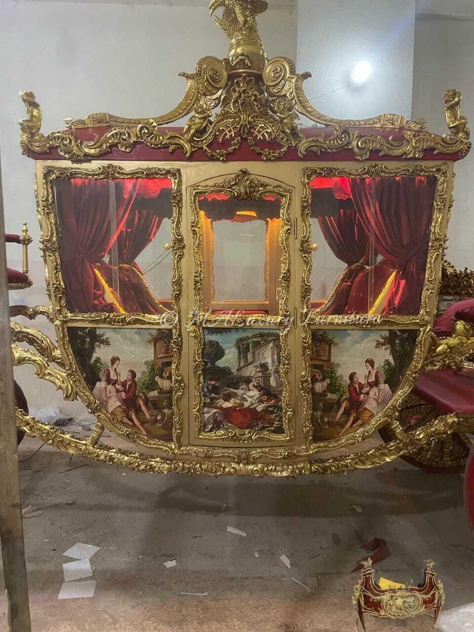 May include: A gold-toned carriage featuring ornate carved detailing, red velvet curtains, and glass windows. The lower panels display painted scenes of figures in period clothing. An eagle figure sits atop the roof, and the structure is framed by intricate gold scrollwork.