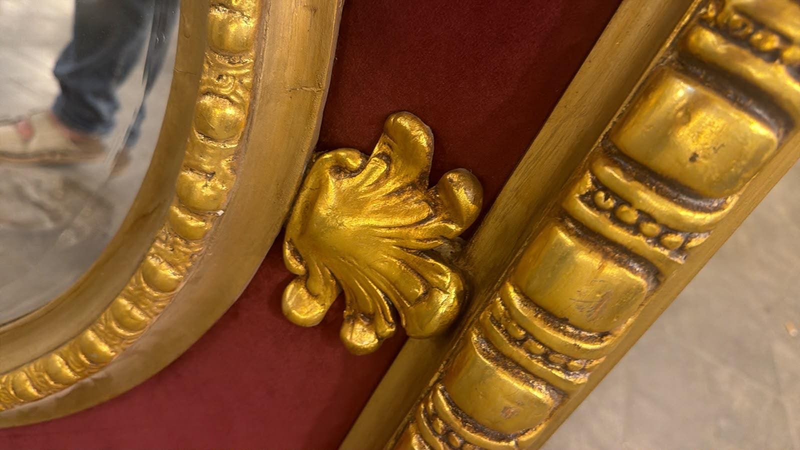 May include: A gold-painted mirror frame featuring a deep red velvet inlay and a prominent gold-colored shell-shaped ornament. The frame is decorated with a repeating beaded pattern along the inner edge and a segmented rectangular design on the outer border.